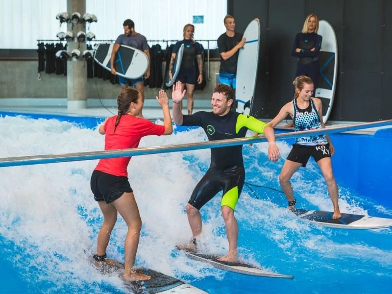 Bild - Drei Menschen surfen auf der Indoor Welle