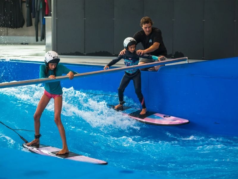 Bild - 2 Kinder surfen mit Hilfe einer Stange auf der stehenden Welle mit einem Instruktor