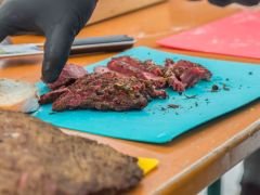 Ein Grillmeister zeigt einer Gruppe von Menschen wie man am besten Fleisch schneidet