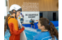 ThumbnailEin Mädchen und eine Surflehrerin sind im Gespräch, während eine weitere Surflehrerin einem anderen Mädchen beim Einstieg auf die stehende Welle hilft
