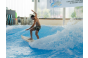 ThumbnailEin Mann surft auf der stehenden Welle in einer Indoor-Anlage der Jochen Schweizer Arena. Er trägt eine Badehose und balanciert auf seinem Surfbrett, während Wasser um ihn herum spritzt.