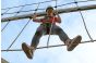 ThumbnailHochseilgarten-Abenteuer in der Jochen Schweizer Arena: Eine Frau mit Helm und Klettergurt erklimmt eine Hängebrücke in luftiger Höhe unter freiem Himmel.