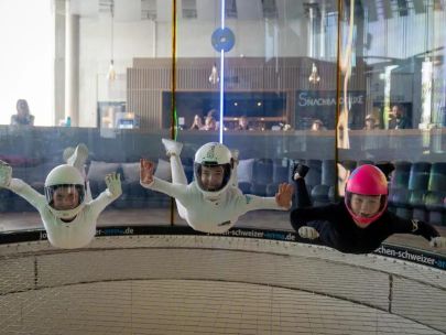Bodyflying in der Jochen Schweizer Arena: Drei Teilnehmer in weißen und schwarzen Anzügen schweben synchron im Windtunnel und demonstrieren Körperkontrolle beim Indoor-Skydiving.