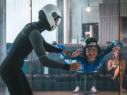 Bodyflying-Erlebnis in der Jochen Schweizer Arena: Eine Teilnehmerin im blauen Fluganzug schwebt im Windtunnel, begleitet von einem erfahrenen Indoor-Skydiving-Instruktor.