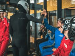 6 Personen und ein Instruktor sind in dem Raum vor dem Windkanal und der Instruktor und ein Kunde klatschen sich ab