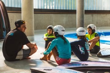 Eine Gruppe von Kindern sitzen bei der Indoor Surfwelle