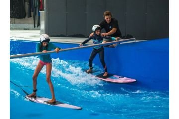 2 Kinder surfen mit Hilfe einer Stange auf der stehenden Welle mit einem Instruktor