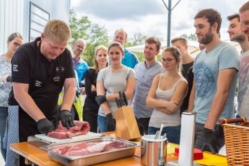 Ein Grillmeister zeigt einer Gruppe von Menschen wie man am besten Fleisch schneidet